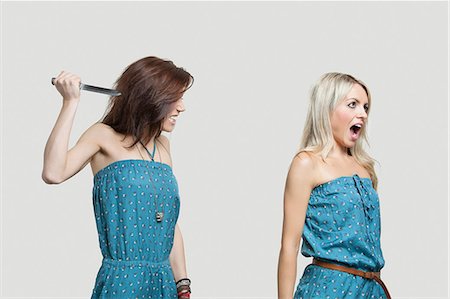 faca - Friend stabbing young woman in similar jump suits from behind Foto de stock - Royalty Free Premium, Número: 693-06380021