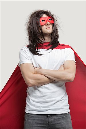 Young man in super hero costume standing with arms crossed against gray background Stock Photo - Premium Royalty-Free, Code: 693-06380066