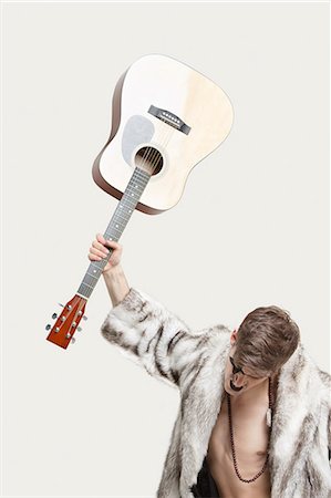Frustrated young man in fur coat about to throw his guitar against gray background Foto de stock - Sin royalties Premium, Código: 693-06380068