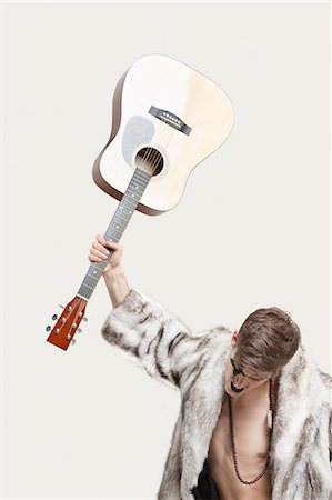 rockstar guitarist - Frustrated young man in fur coat about to throw his guitar against gray background Stock Photo - Premium Royalty-Free, Code: 693-06380068