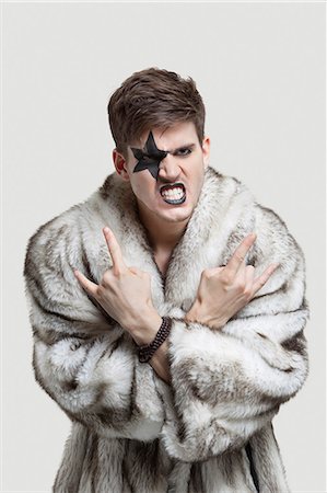 Portrait of frustrated young man in fur coat clenching teeth and making rebellious gesture against gray background Stock Photo - Premium Royalty-Free, Code: 693-06380070
