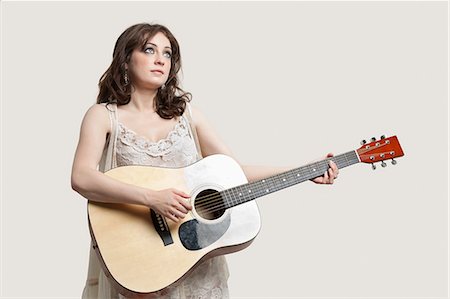 Jeune femme regardant vers le haut tout en jouant la guitare sur fond gris Photographie de stock - Premium Libres de Droits, Code: 693-06380073