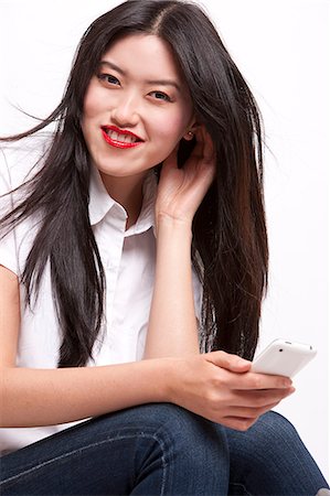 Portrait of cheerful young woman in casuals using mobile phone over white background Stock Photo - Premium Royalty-Free, Code: 693-06403186