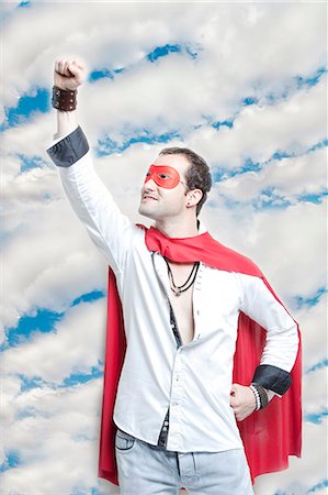 fantasy (not sexual) - Young man in superhero costume with hand raised against cloudy sky Stock Photo - Premium Royalty-Free, Code: 693-06403199