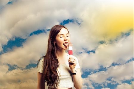 enjoying ice cream - Belle jeune femme léchant popsicle sur fond de ciel nuageux Photographie de stock - Premium Libres de Droits, Code: 693-06403192