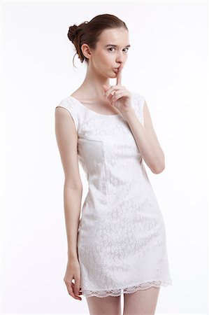 secret (mysterious or hidden) - Young woman in dress gesturing to be quiet over white background Foto de stock - Sin royalties Premium, Código: 693-06403256