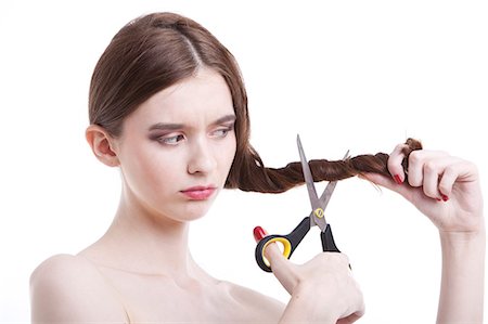 Sad young woman with scissors cutting her hair over white background Stock Photo - Premium Royalty-Free, Code: 693-06403265