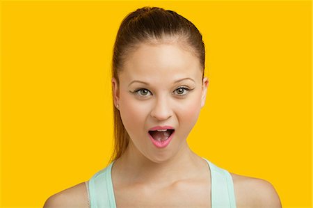 Portrait of surprised young woman with mouth open over yellow background Stock Photo - Premium Royalty-Free, Code: 693-06403275