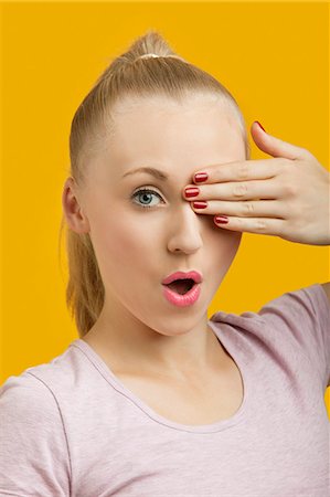 schock - Porträt einer schönen jungen Frau, die ein Auge über gelbem Hintergrund Stockbilder - Premium RF Lizenzfrei, Bildnummer: 693-06403279