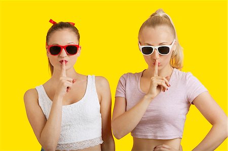 silence sign - Portrait of two playful young women with fingers on lips over yellow background Stock Photo - Premium Royalty-Free, Code: 693-06403285