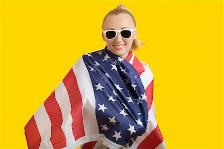 digno - Portrait of happy young woman wrapped in American flag over yellow background Foto de stock - Sin royalties Premium, Código: 693-06403287