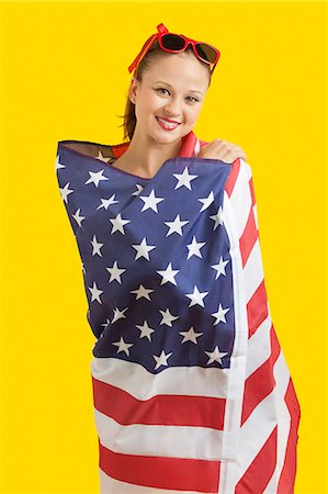 digno - Portrait of happy young woman wrapped in American flag over yellow background Foto de stock - Sin royalties Premium, Código: 693-06403289