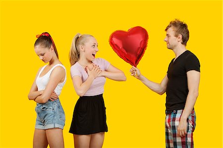 dating - Young man gifting heart shaped balloon to surprised woman with friend feeling left out standing behind Foto de stock - Sin royalties Premium, Código: 693-06403304