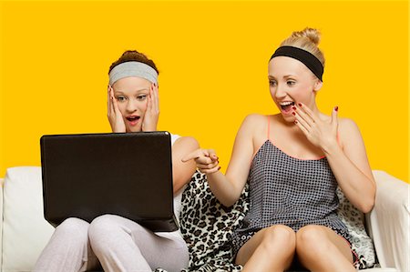 surprise point - Two shocked young women using laptop sitting on sofa against yellow background Foto de stock - Sin royalties Premium, Código: 693-06403308