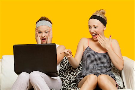 erstaunlich - Zwei schockiert junge Frauen mit Laptop sitzen auf dem Sofa vor gelbem Hintergrund Stockbilder - Premium RF Lizenzfrei, Bildnummer: 693-06403308