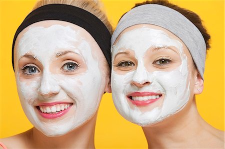 Portrait of two happy women with face pack on their faces over yellow background Foto de stock - Royalty Free Premium, Número: 693-06403309