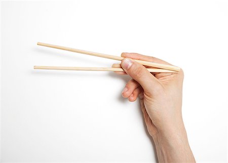 palillo (oriental) - Man's hand gripping chopsticks over white background Foto de stock - Sin royalties Premium, Código: 693-06403363