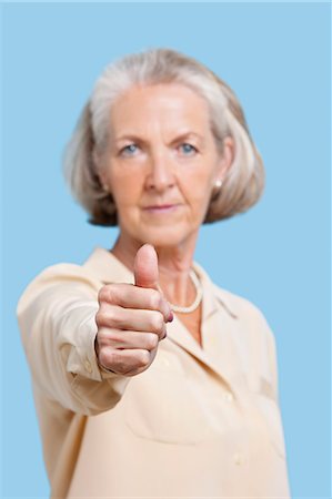 Portrait of senior woman in casuals gesturing thumbs up against blue background Stock Photo - Premium Royalty-Free, Code: 693-06403410