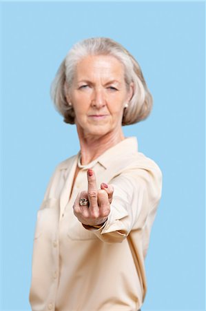 simsearch:6108-06167263,k - Portrait of senior woman in casuals making rebellious gesture against blue background Stock Photo - Premium Royalty-Free, Code: 693-06403412