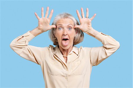 silly lady - Portrait of senior woman making funny faces with hands on head against blue background Foto de stock - Sin royalties Premium, Código: 693-06403413