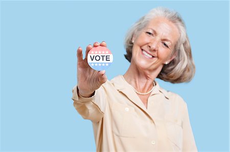 people government - Portrait of senior woman holding an election badge against blue background Stock Photo - Premium Royalty-Free, Code: 693-06403427