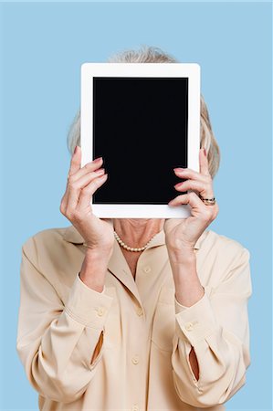 Haute femme tenant des tablet PC en face de son visage sur fond bleu Photographie de stock - Premium Libres de Droits, Code: 693-06403435