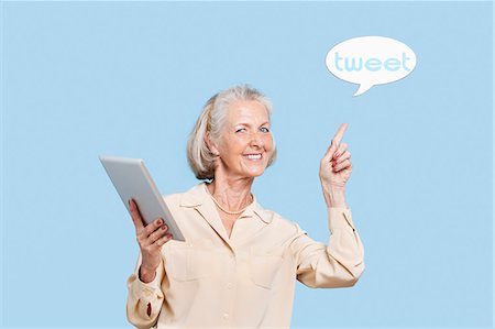 social media - Portrait of senior woman with tablet PC pointing at tweet bubble against blue background Stock Photo - Premium Royalty-Free, Code: 693-06403436