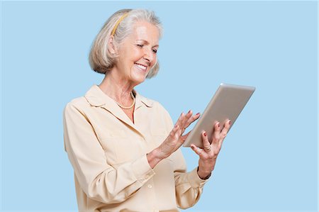 Happy senior woman using tablet PC against blue background Foto de stock - Sin royalties Premium, Código: 693-06403431