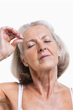 Senior woman tweezing eyebrows against white background Stock Photo - Premium Royalty-Free, Code: 693-06403452