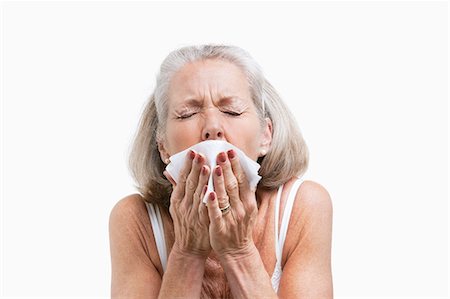 senior woman head and shoulders not smiling - Senior woman sneezing into a tissue against white background Stock Photo - Premium Royalty-Free, Code: 693-06403460
