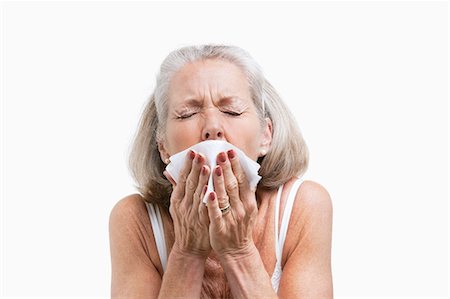 sick senior - Senior woman sneezing into a tissue against white background Stock Photo - Premium Royalty-Free, Code: 693-06403460