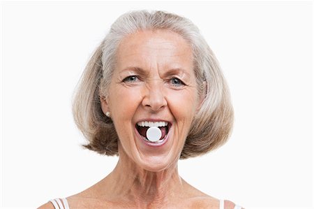 Portrait of senior woman with pill between her teeth against white background Stock Photo - Premium Royalty-Free, Code: 693-06403462