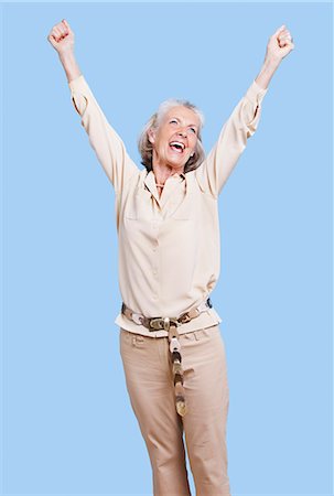 Excited senior woman in casuals cheering with arms raised against blue background Stock Photo - Premium Royalty-Free, Code: 693-06403478