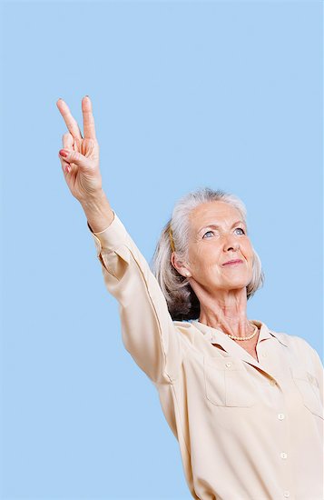 Senior woman in casuals gesturing peace sign against blue background Foto de stock - Sin royalties Premium, Código de la imagen: 693-06403479