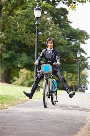 simsearch:693-06403504,k - Portrait of young businessman riding bicycle with legs kicked out Stock Photo - Premium Royalty-Free, Code: 693-06403491