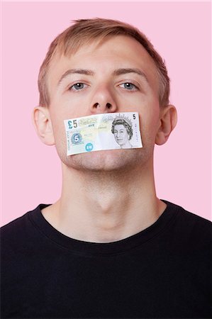 funny man looking at camera - Portrait of a young man with paper money stuck over his mouth against pink background Stock Photo - Premium Royalty-Free, Code: 693-06403529