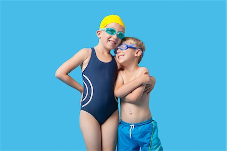 Happy young siblings in swimwear with arm around over blue background Fotografie stock - Premium Royalty-Free, Codice: 693-06403574