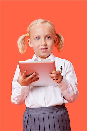 Portrait of a happy young schoolgirl holding tablet PC over orange background Stock Photo - Premium Royalty-Free, Code: 693-06403584