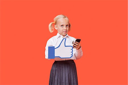 education communications - Portrait of a young schoolgirl with cell phone holding fake like button over orange background Stock Photo - Premium Royalty-Free, Code: 693-06403587