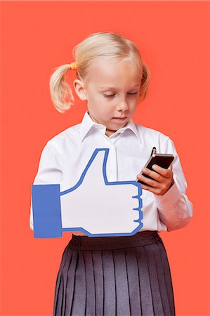 simsearch:614-06974081,k - Young schoolgirl with cell phone holding fake like button against orange background Stock Photo - Premium Royalty-Free, Code: 693-06403588