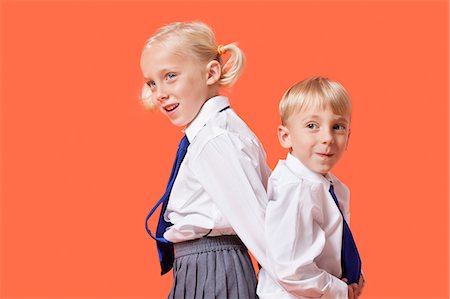 Happy young boy and girl in school uniform standing back to back over orange background Stock Photo - Premium Royalty-Free, Code: 693-06403593