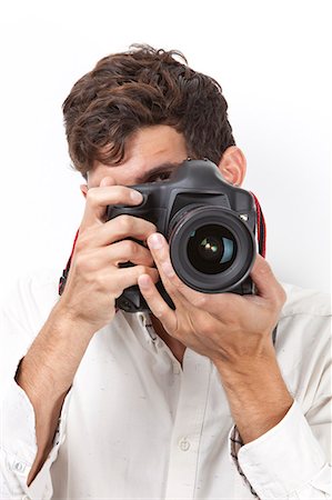 Young man taking photograph with vintage camera against white background Stock Photo - Premium Royalty-Free, Code: 693-06435757
