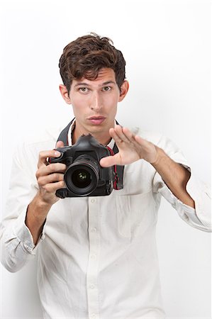 photos nostalgia - Portrait of young photographer with vintage camera gesturing against white background Stock Photo - Premium Royalty-Free, Code: 693-06435758