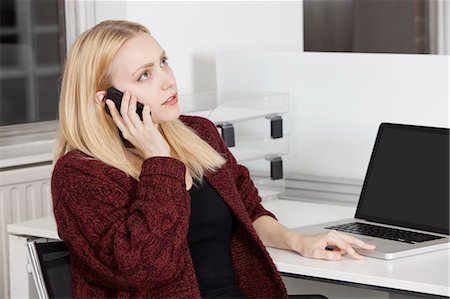 simsearch:693-06403498,k - Young businesswoman using cell phone while sitting at desk in office Stock Photo - Premium Royalty-Free, Code: 693-06435792