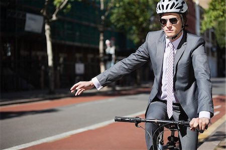 Jeune homme d'affaires montrant des signes de la main alors qu'il circulait à vélo Photographie de stock - Premium Libres de Droits, Code: 693-06435821