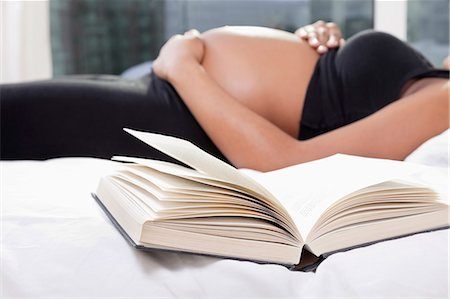 female sports bra - Mid section of pregnant woman lying in bed with open book in foreground Stock Photo - Premium Royalty-Free, Code: 693-06435852