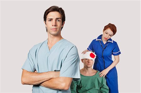 exames de sangue - Portrait of male doctor with female nurse treating an injured patient against gray background Foto de stock - Royalty Free Premium, Número: 693-06435914