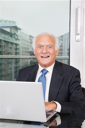 simsearch:693-06403504,k - Portrait of happy elderly businessman with laptop sitting at table Stock Photo - Premium Royalty-Free, Code: 693-06435940