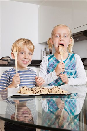 Portrait of happy boy with sister tasting spatula mix with cookie batter in kitchen Stock Photo - Premium Royalty-Free, Code: 693-06435987