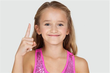 Portrait of young girl pointing upwards against gray background Stock Photo - Premium Royalty-Free, Code: 693-06436028